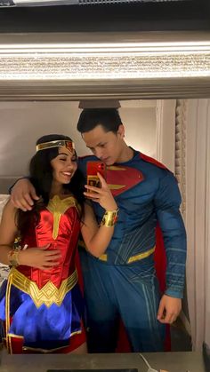 a man and woman dressed as superman and wondergirl standing in front of a mirror