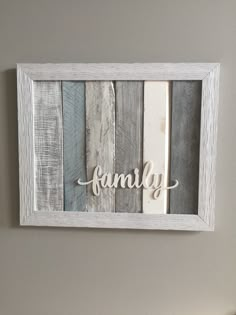 a wooden frame with the word family painted on it in white and grey colors, hanging above a bed