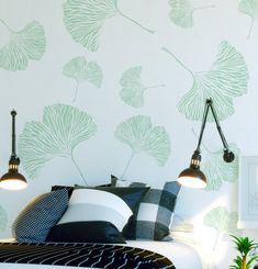 a bed sitting under two lamps next to a wall with green leaves painted on it