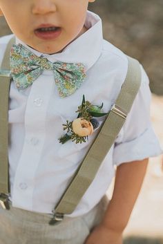 a young boy wearing a bow tie and suspenders with flowers on the lapel