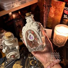 a person holding up a glass bottle with an ornate design on it and some candles in the background