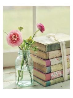 a vase filled with pink flowers sitting on top of a table next to stacks of books