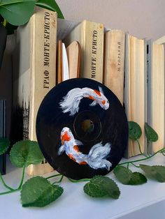 two koi fish painted on a black disc next to books and plants in a vase