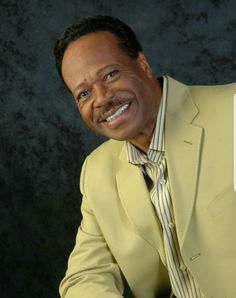 a man in a yellow suit and striped shirt smiling at the camera with his hands on his knees