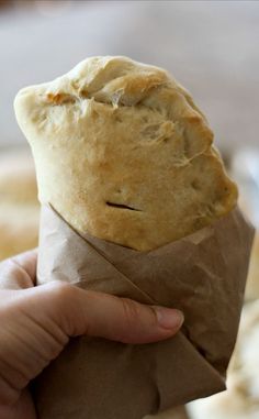 a hand holding a piece of bread wrapped in brown paper with a bite taken out of it