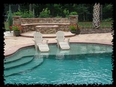 two lawn chairs sitting on top of a swimming pool next to a stone fire pit