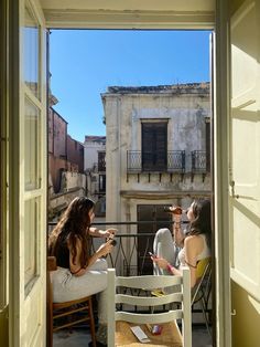 two women sitting at a table on an open balcony looking out onto the city below