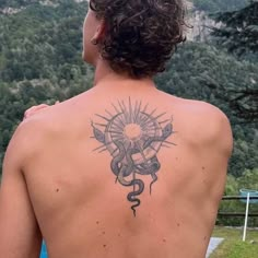 a man with a tattoo on his back is looking out at the mountains and trees