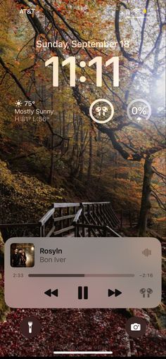 an iphone screen with the music player on it's side and trees in the background