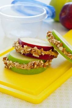 an apple sandwich with granola and apples on a yellow cutting board next to plastic containers