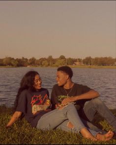 two young people sitting on the grass near a body of water, one smiling at the camera