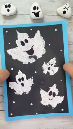 someone is holding up a black and white paper with ghost faces on it, while three small rocks are in the background