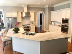 a large kitchen with an island in the middle and white cabinets on both sides, along with stainless steel appliances