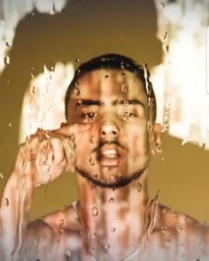 a man with his hand on his face in front of a window that has water drops all over it