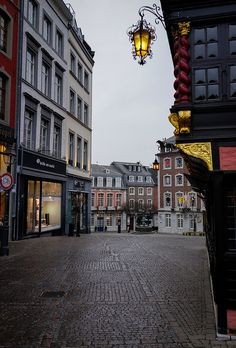 an empty cobblestone street in the middle of some old european buildings with lights hanging from them