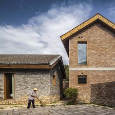 a man standing in front of a brick building holding a mop and wearing a straw hat