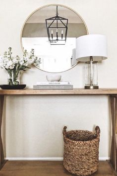 a table with a mirror, lamp and basket sitting on it's sideboard