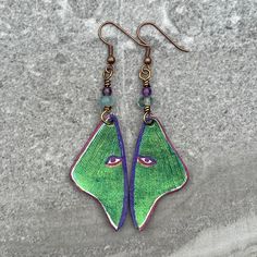 a pair of earrings with green and purple designs on them sitting on a rock surface