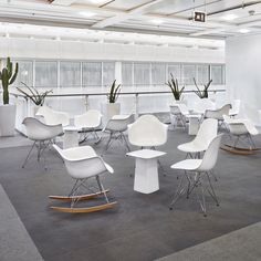 a room filled with lots of white chairs next to plants and paintings on the wall