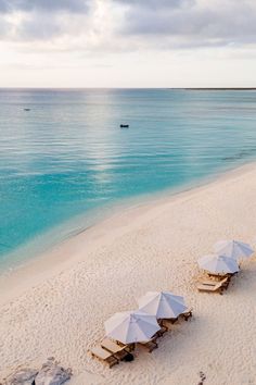 several umbrellas and chairs on the beach with clear blue water in the back ground