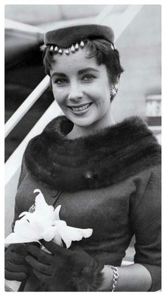 a black and white photo of a woman in a fur stoler holding a flower