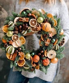 a woman holding a christmas wreath with oranges and other decorations