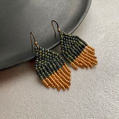 the beaded earrings are hanging from hooks on a plate with a black and gold background