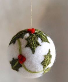 a white ornament with holly leaves and red berries hanging from a gold chain