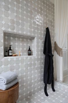 a white tiled bathroom with shelves and towels on the wall, along with a wooden stool