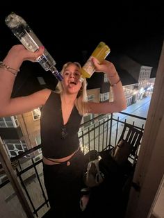 a woman is holding two bottles in her hands and posing for the camera at night