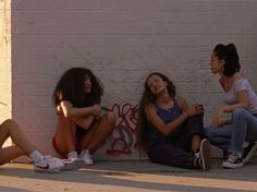 three young women sitting on the ground next to a wall