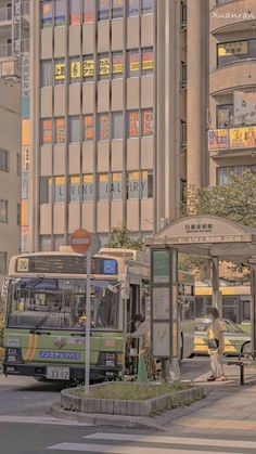 two buses parked at a bus stop in front of tall buildings