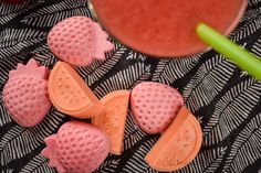 some fruit shaped soaps next to a cup of watermelon and a green straw