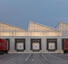 three red semi trucks parked in front of an industrial building with two doors on each side