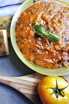 a bowl of stew next to a slice of cheese and a tomato