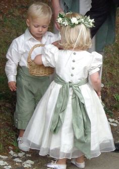 two young children dressed in white and green outfits, one holding a basket while the other holds