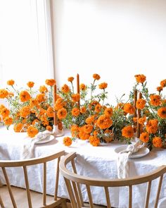 the table is set with white linens and orange flowers in vases on them