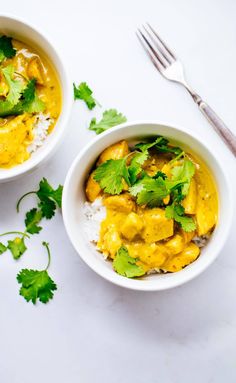 two white bowls filled with yellow curry and cilantro garnished with parsley