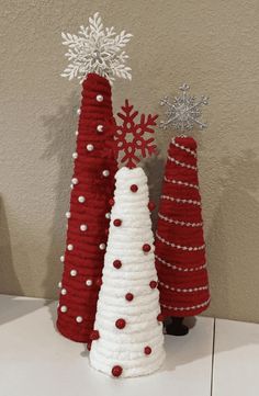 three knitted christmas trees sitting on top of a white table next to each other