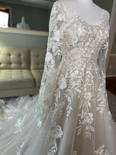 a white wedding dress on display in a room with a couch and window behind it