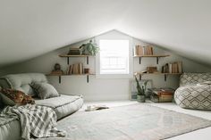 a living room filled with furniture and bookshelves next to a large window on top of a slanted wall