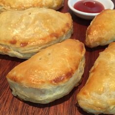 four pastries sitting on top of a wooden table next to a bowl of ketchup