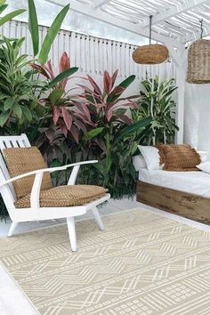 an outdoor area with two white chairs and some plants on the wall, in front of a bed