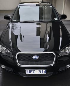 the front end of a black car parked in a parking lot next to a building