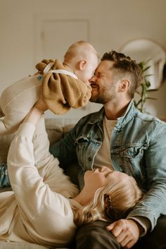 a man and woman are sitting on a couch with a baby in their lap as they kiss each other