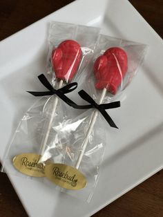 two red lollipops wrapped in cellophane on a white square plate