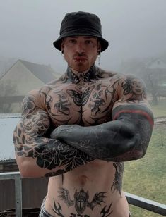 a man with tattoos on his chest and arms is standing in front of a fence