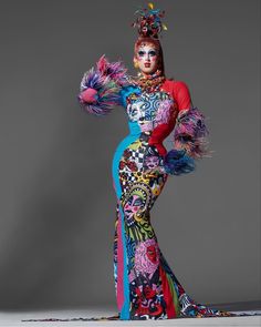 a woman in a colorful dress with feathers on her head and arms, posing for the camera