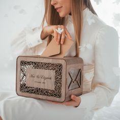 a woman in white holding a wooden box with an ornament on the front