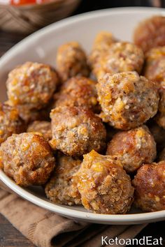 a white bowl filled with meatballs sitting on top of a wooden table next to a napkin